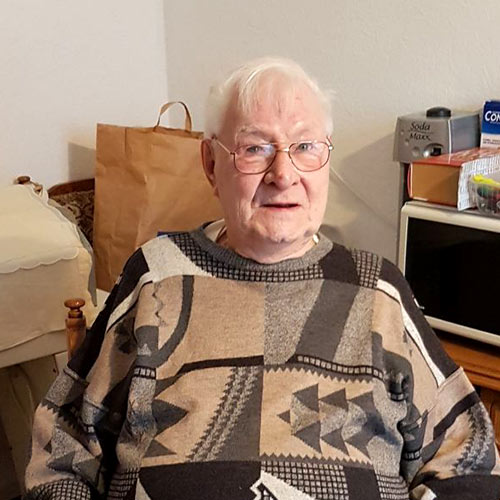 Ein alter Herr sitzt in einem Rollstuhl in seiner Wohnung und sinniert über seine Zufriedenheit.