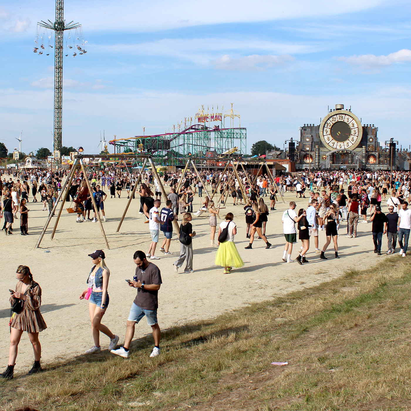 Auf einem Festivalgelände gehen Menschen in lockerer Atmosphäre über eine Sandfläche