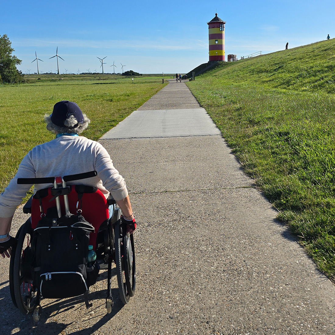 Eine Dame im Rollstuhl genießt ihren Individualurlaub an der Nordsee. Sie steuert mit Ihrem Rollstuhl auf den Berühmten 'Otto-Leuchtturm' zu.