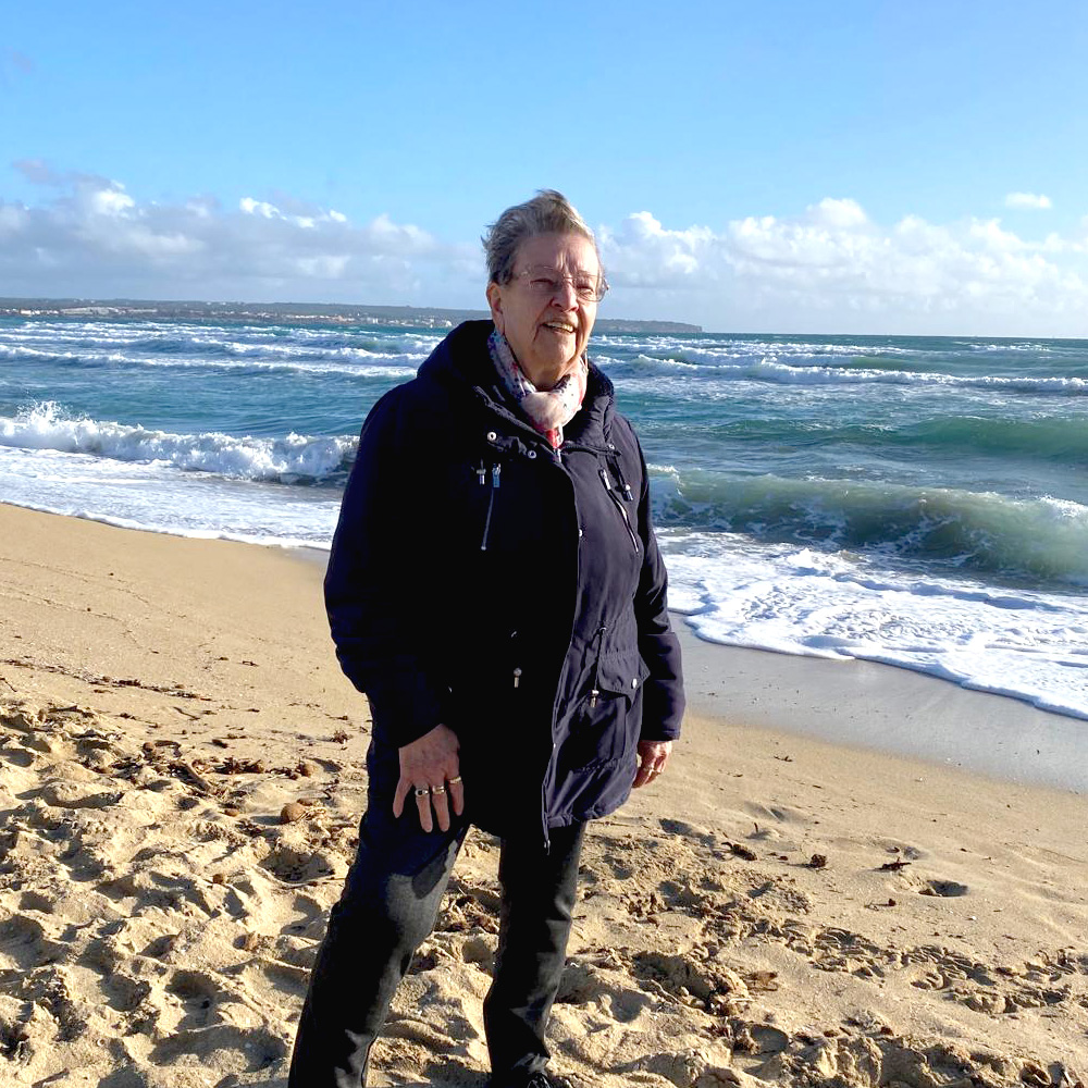 Eine rüstige ältere Dame steht am Strand von Mallorca und genießt die Meeresbrise.